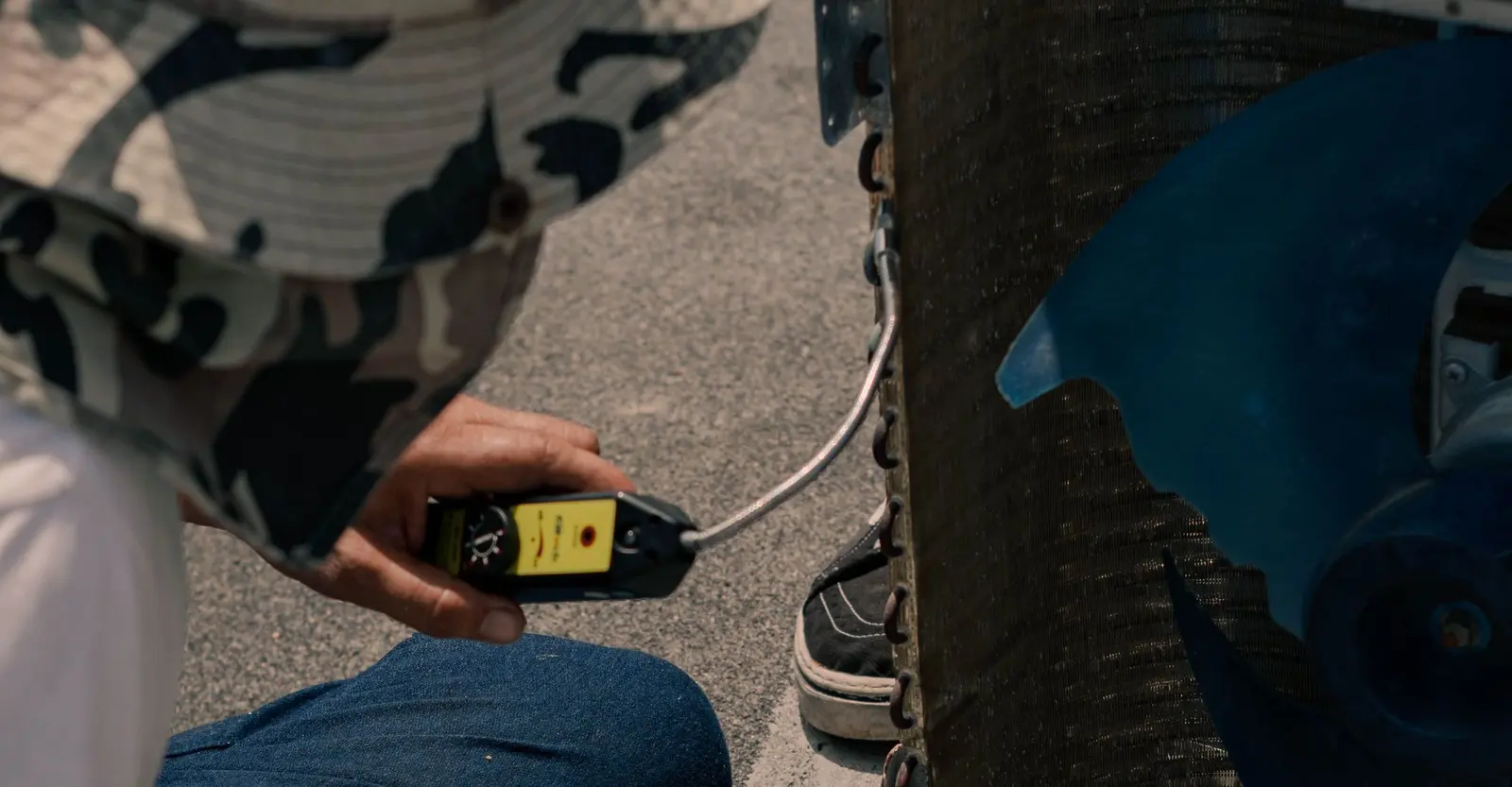 Technician's hand holding a leak detector against the coil of an air conditioning unit